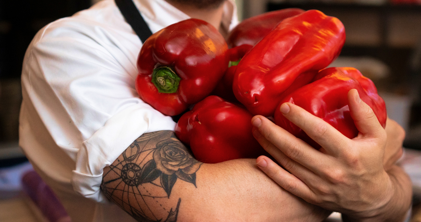 A man in an apron carrying red peppers in his arms