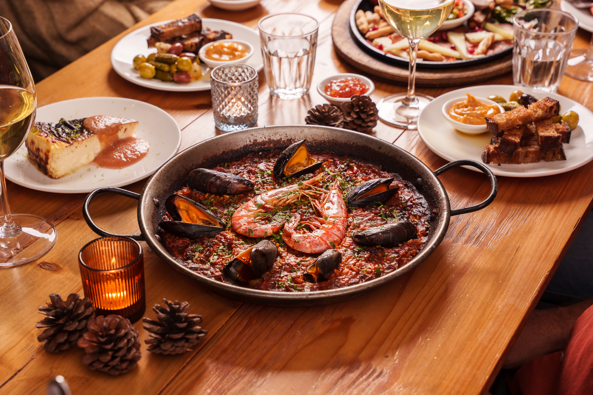 A close-up of a traditional arroz horno dish, featuring prawns and mussels served in a rustic pan surrounded by tapas.
